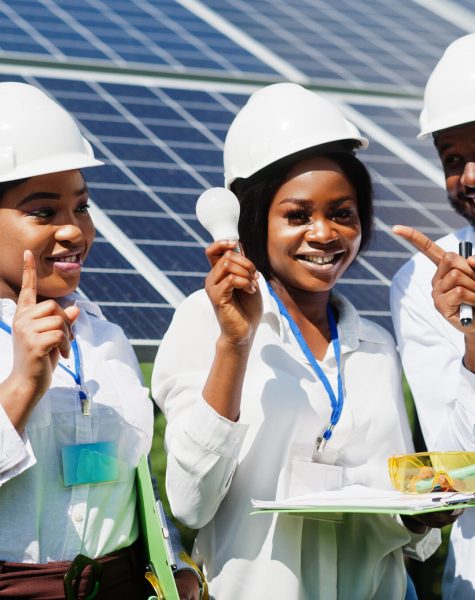 African american technician checks the maintenance of the solar African american technician checks the maintenance of the solar panels. Group of three black engineers meeting at solar station. Hold led bulb.