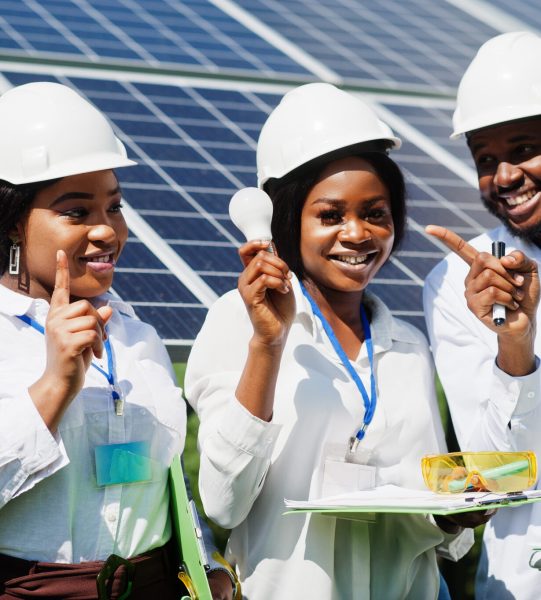 African american technician checks the maintenance of the solar panels. Group of three black engineers meeting at solar station. Hold led bulb.