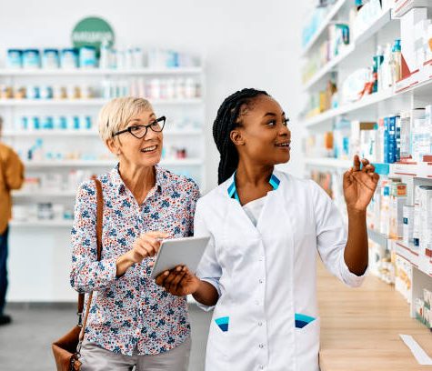 African American female pharmacist and her senior customer using touchpad while searching for a medicine in drugstore.