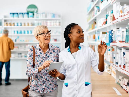 African American female pharmacist and her senior customer using touchpad while searching for a medicine in drugstore.