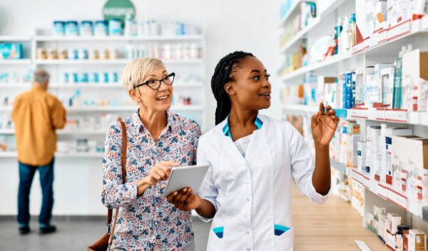 African American female pharmacist and her senior customer using touchpad while searching for a medicine in drugstore.
